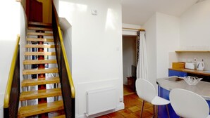 Una escalera con barandilla de madera que lleva a una habitación con zona de cocina, que incluye una encimera, sillas y un radiador.
