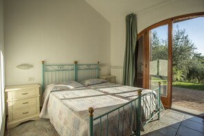 Une chambre à coucher comprenant un lit, une table de chevet, une commode et une grande fenêtre donnant sur l’extérieur.