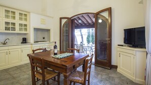 A kitchen with a wooden dining table, chairs, cabinets, and a television.