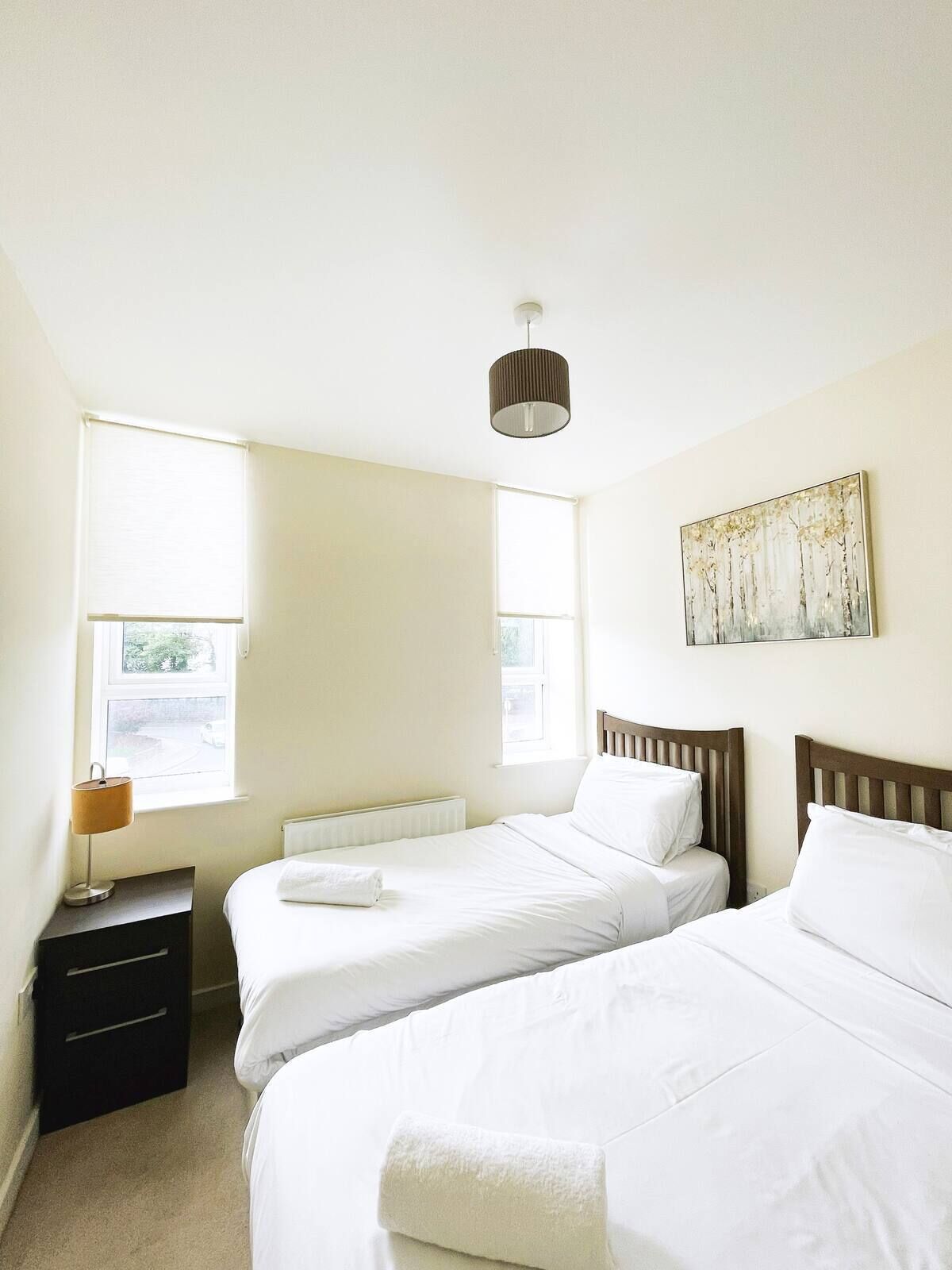 Una camera da letto con due letti, un termosifone, una lampada e un quadro appeso al muro.