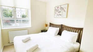 A neatly made bed with white linens, a wooden headboard, and a single bedside lamp. - Golden Heights 7 (Maidstone)