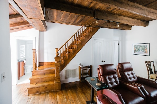 Un escalier en bois menant à un deuxième étage, un fauteuil en cuir et un tableau encadré au mur.
