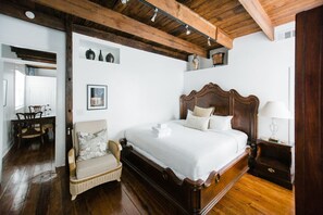 Une chambre à coucher avec un lit en bois, un fauteuil en osier, une table de chevet avec une lampe et un tableau encadré au mur.
