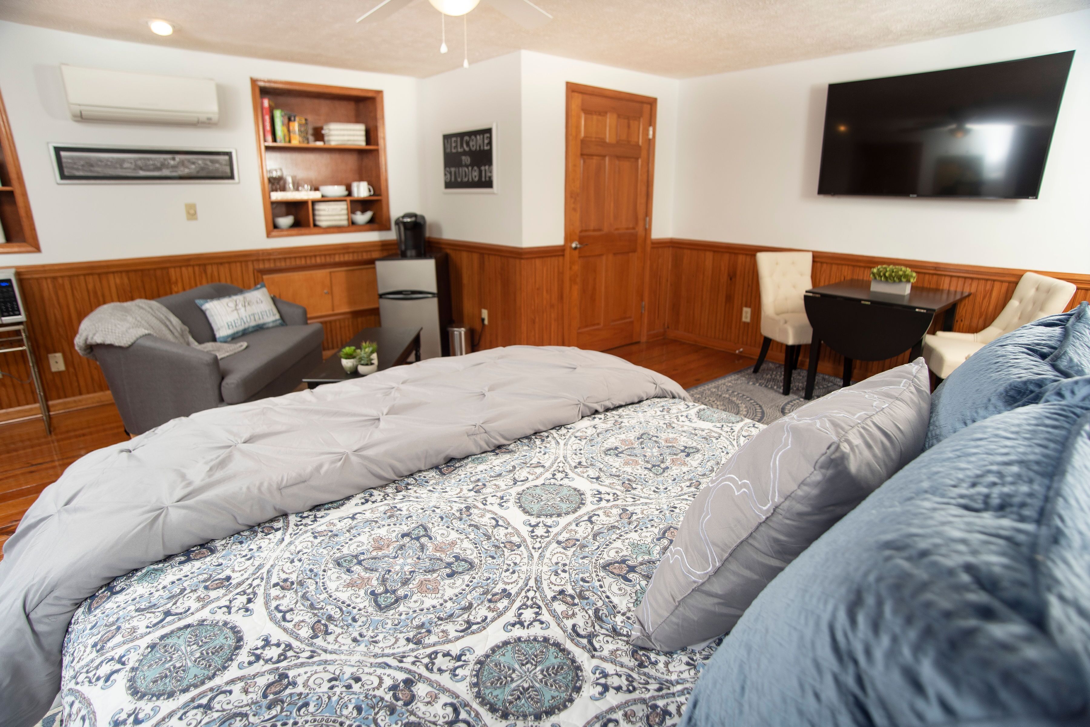 A bedroom with a large bed, a desk, a chair, and a television on the wall.