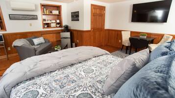 A bedroom with a large bed, a desk, a chair, and a television on the wall.