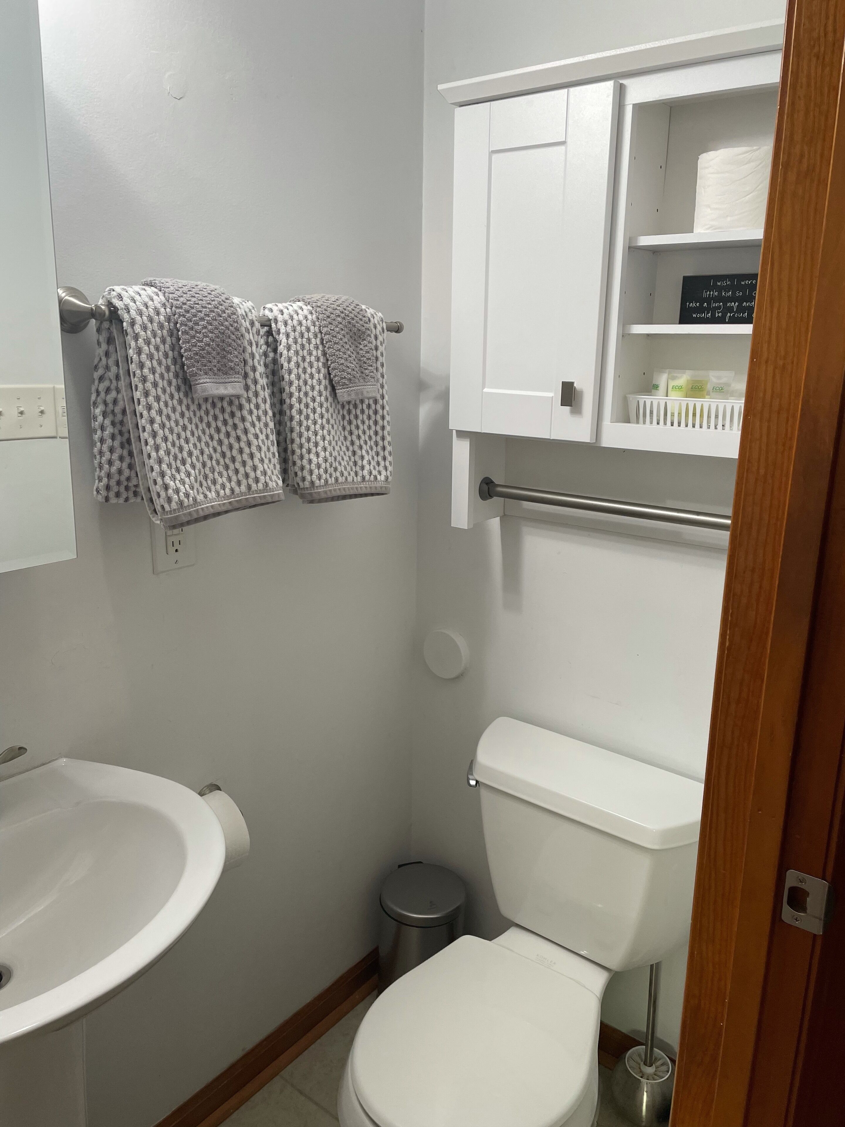 Een kleine badkamer met een witte wastafel, toilet en een kastje met toiletartikelen.