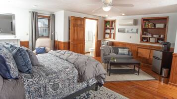 A well-lit room with a bed, a sofa, a coffee table, and a kitchen area with a refrigerator and a microwave.