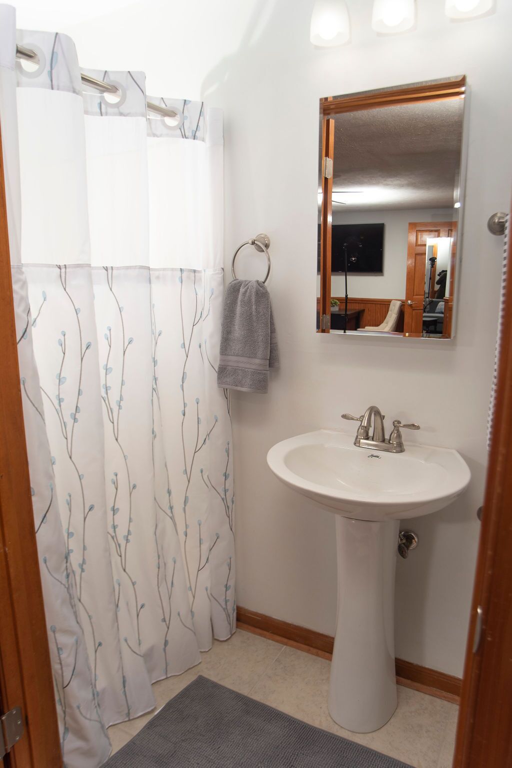 A bathroom with a white sink, a mirror, and a shower curtain with a tree pattern.