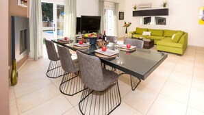 A modern living room with a green sofa, a dining table with chairs, and a flat-screen TV. - EMILY - 3Bed Villa within walking distance to FIG TREE BAY BEACH (Paralimni)
