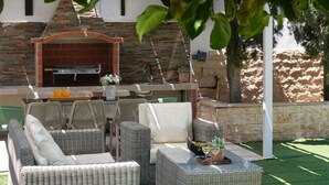 An outdoor seating area with wicker furniture, a grill, and a stone wall. - EMILY - 3Bed Villa within walking distance to FIG TREE BAY BEACH (Paralimni)