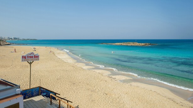 A beach with clear turquoise water, a sign for Fig Tree Bay Watersports, and a sandy shoreline. - EMILY - 3Bed Villa within walking distance to FIG TREE BAY BEACH (Paralimni)