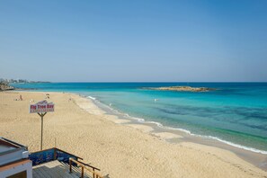 Una playa con agua turquesa cristalina, un letrero de Fig Tree Bay Watersports y una orilla arenosa.