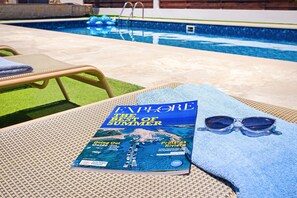 Una rivista su un asciugamano, occhiali da sole e una sedia a bordo piscina.