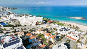 A coastal town with a beach, buildings with solar panels, and a clear blue sea. - EMILY - 3Bed Villa within walking distance to FIG TREE BAY BEACH (Paralimni)