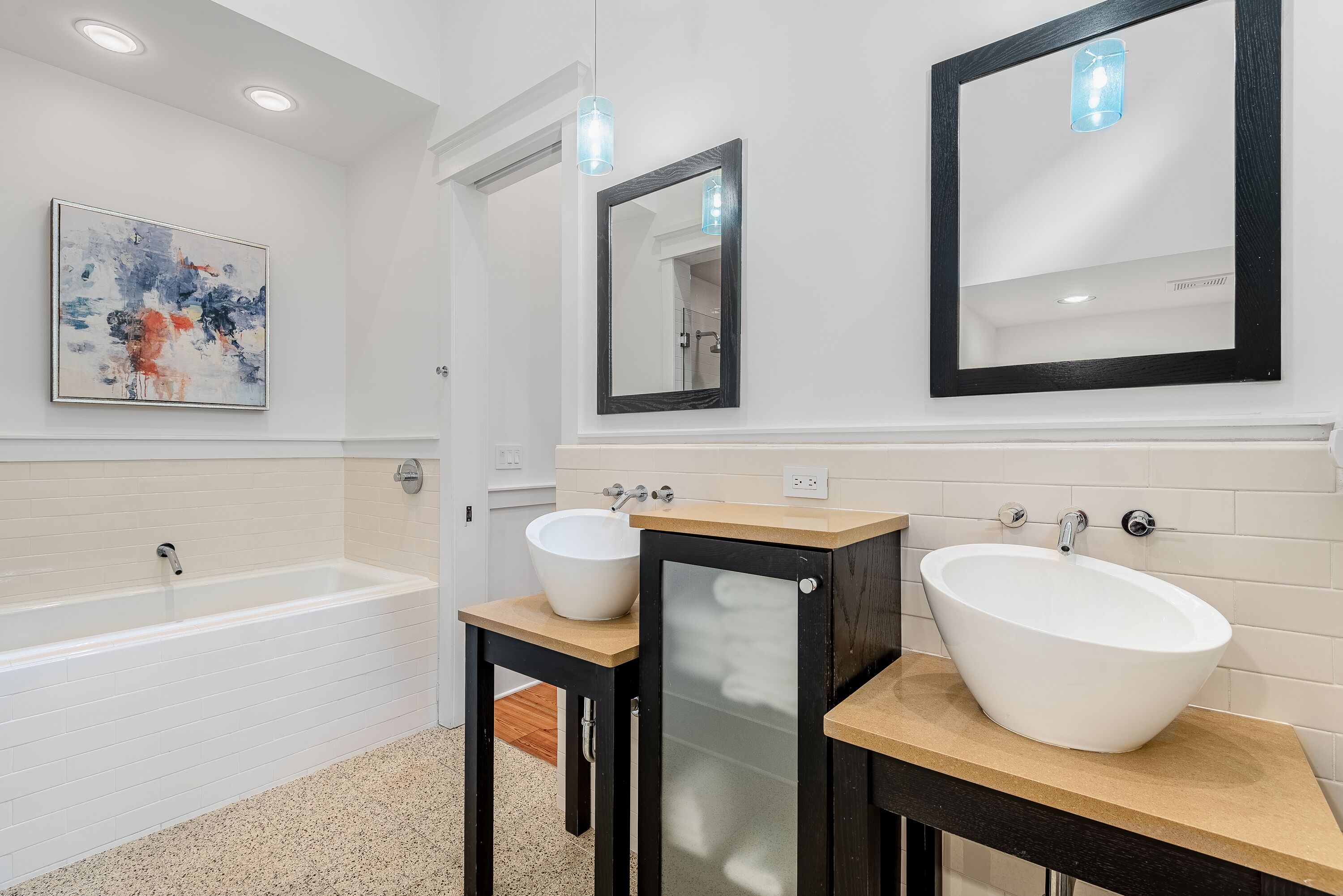 Une salle de bain moderne avec une baignoire sur pieds, deux vasques et un grand tableau abstrait accroché au mur.