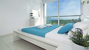 A modern bedroom with a large bed, a view of the city, and a balcony. - Erika Apartment with Panoramic Sea View in Coralli (Paralimni)