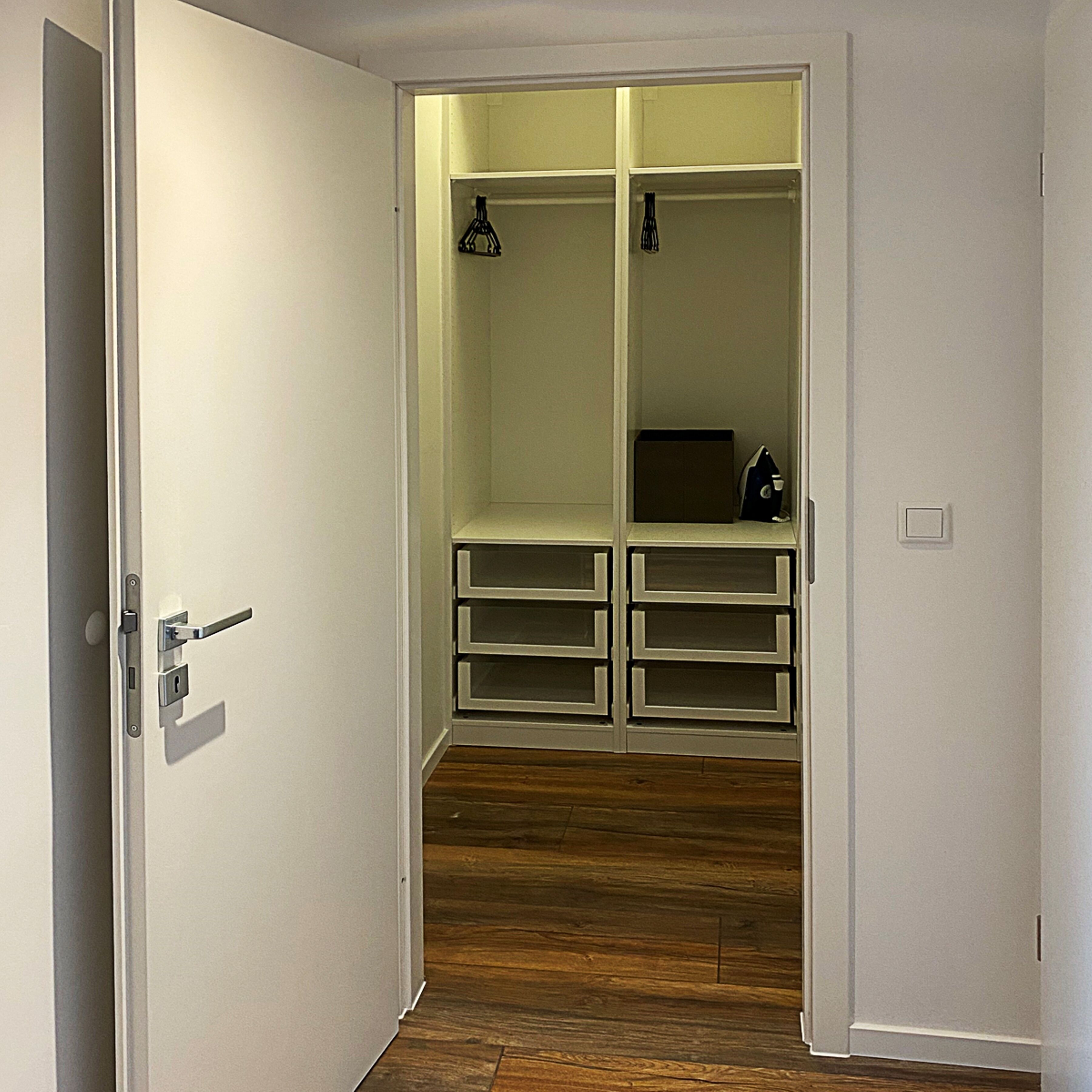 Un closet amplio con puertas abiertas, piso de madera y un picaporte metálico.