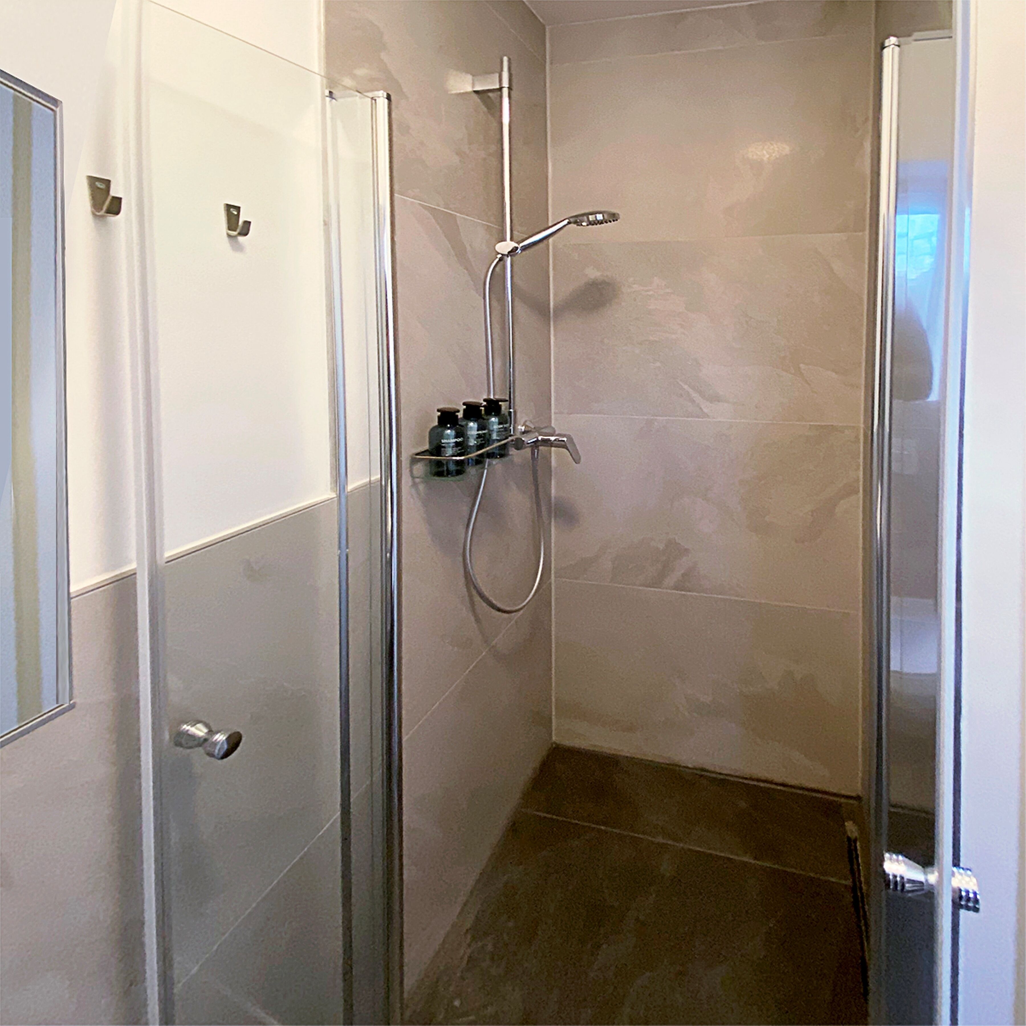 A glass-enclosed shower with a handheld showerhead and a wall-mounted faucet.