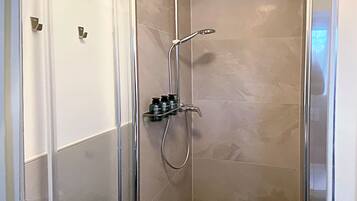 A glass-enclosed shower with a handheld showerhead and a wall-mounted faucet.
