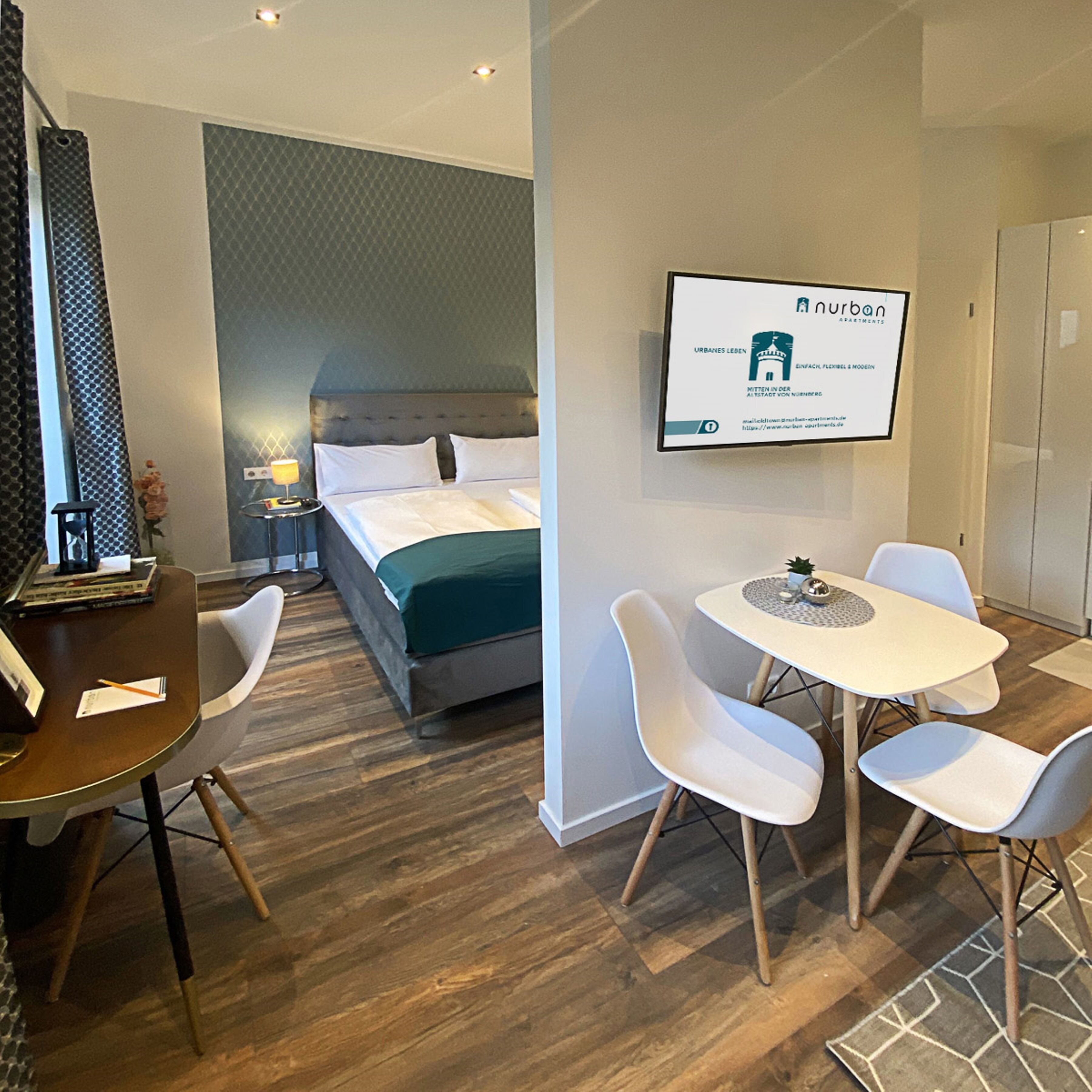 A modern hotel room with a bed, bedside table, lamp, and a dining area with chairs and a table.