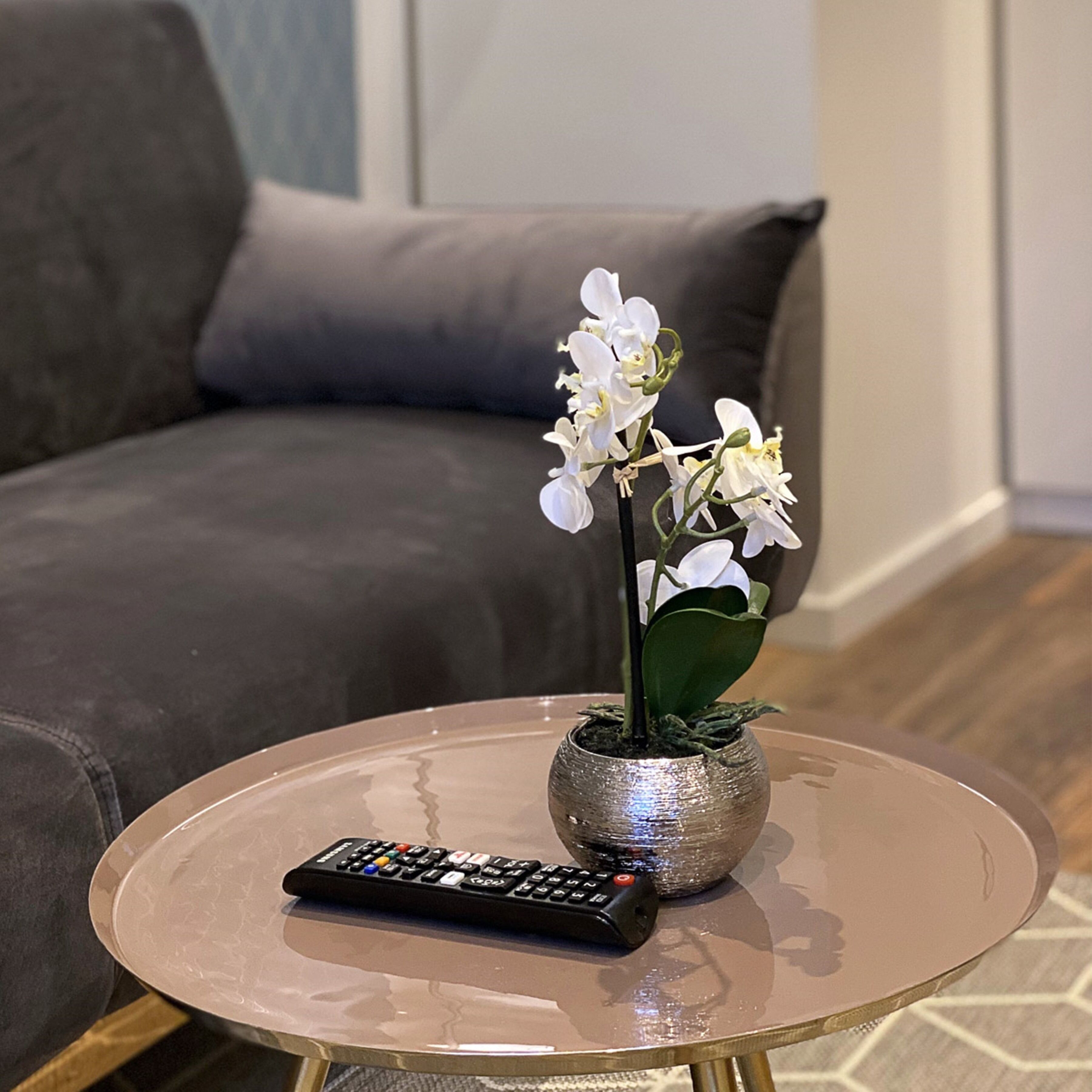A remote control on a round glass coffee table with a potted orchid beside it.