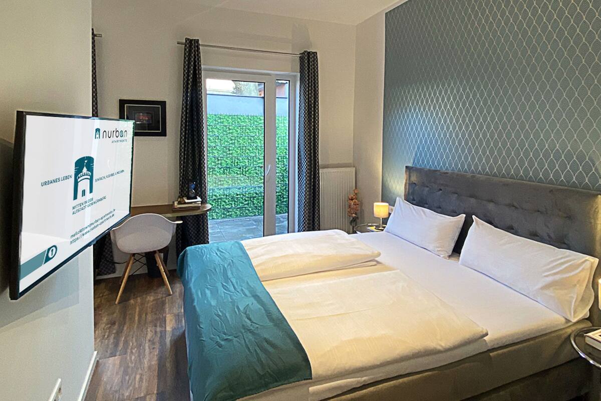 Habitación de hotel con una cama grande, un escritorio, una silla y un televisor mostrando un sitio web.