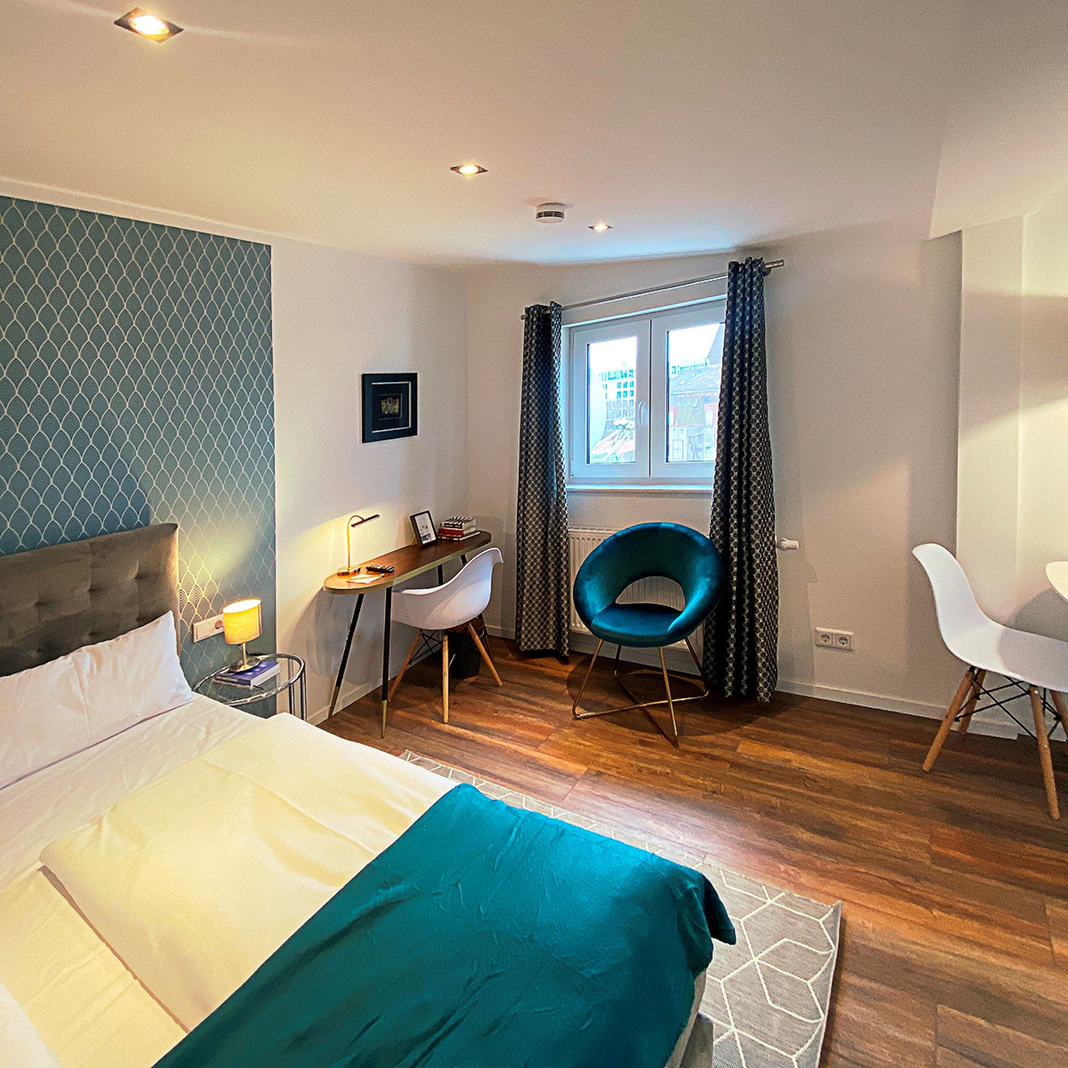 A modern hotel room with a large bed, a desk with a chair, a window with curtains, and a view of the city.