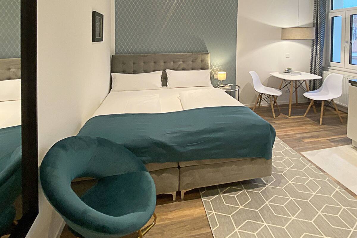 Habitación de hotel moderna con una cama grande, una zona de estar con una mesa y sillas, y vistas al exterior a través de la ventana.