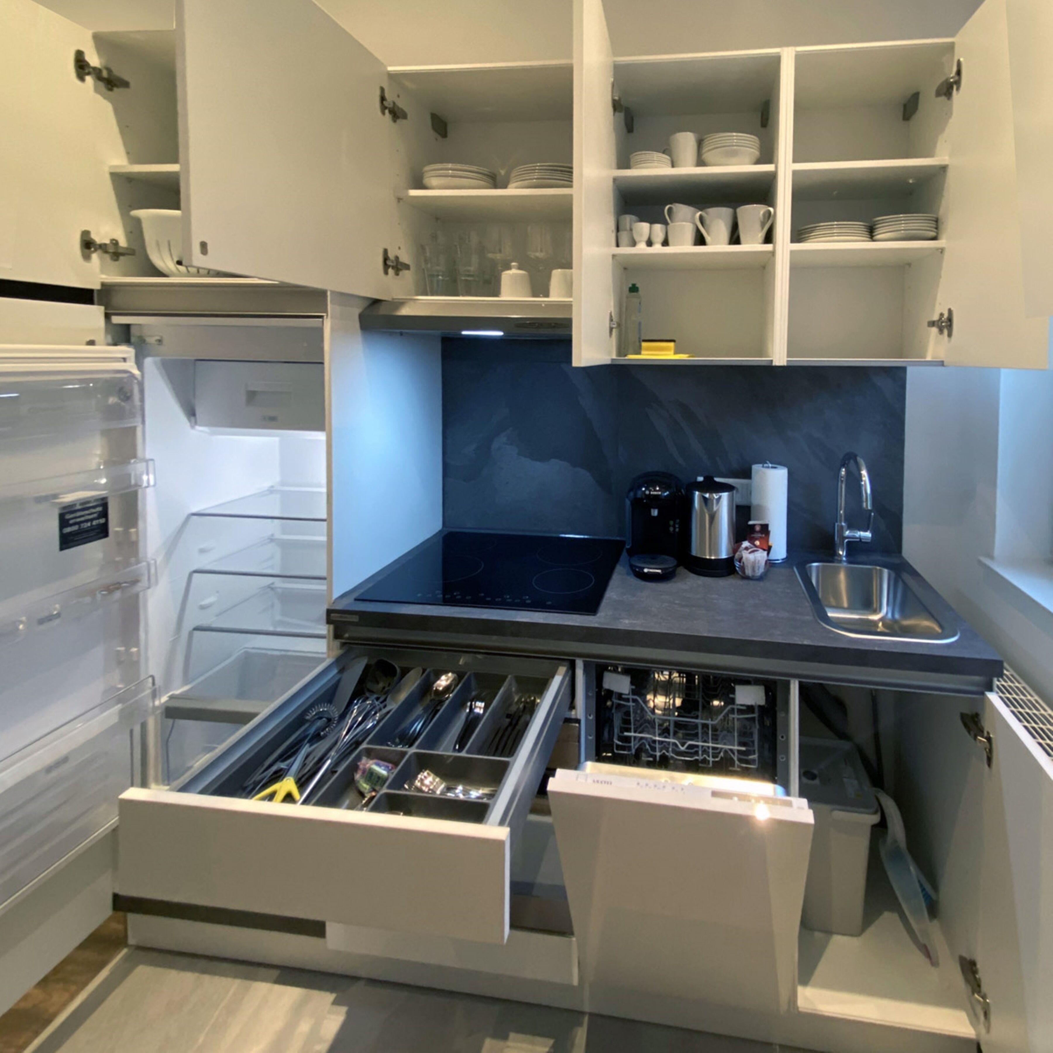 A modern kitchen with built-in appliances, a dishwasher, and a variety of utensils and cookware stored in a drawer.