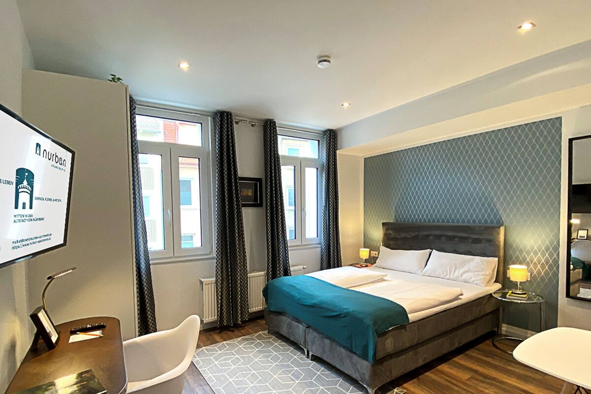 Habitación de hotel con una cama, un escritorio, una silla, una mesita y un televisor.