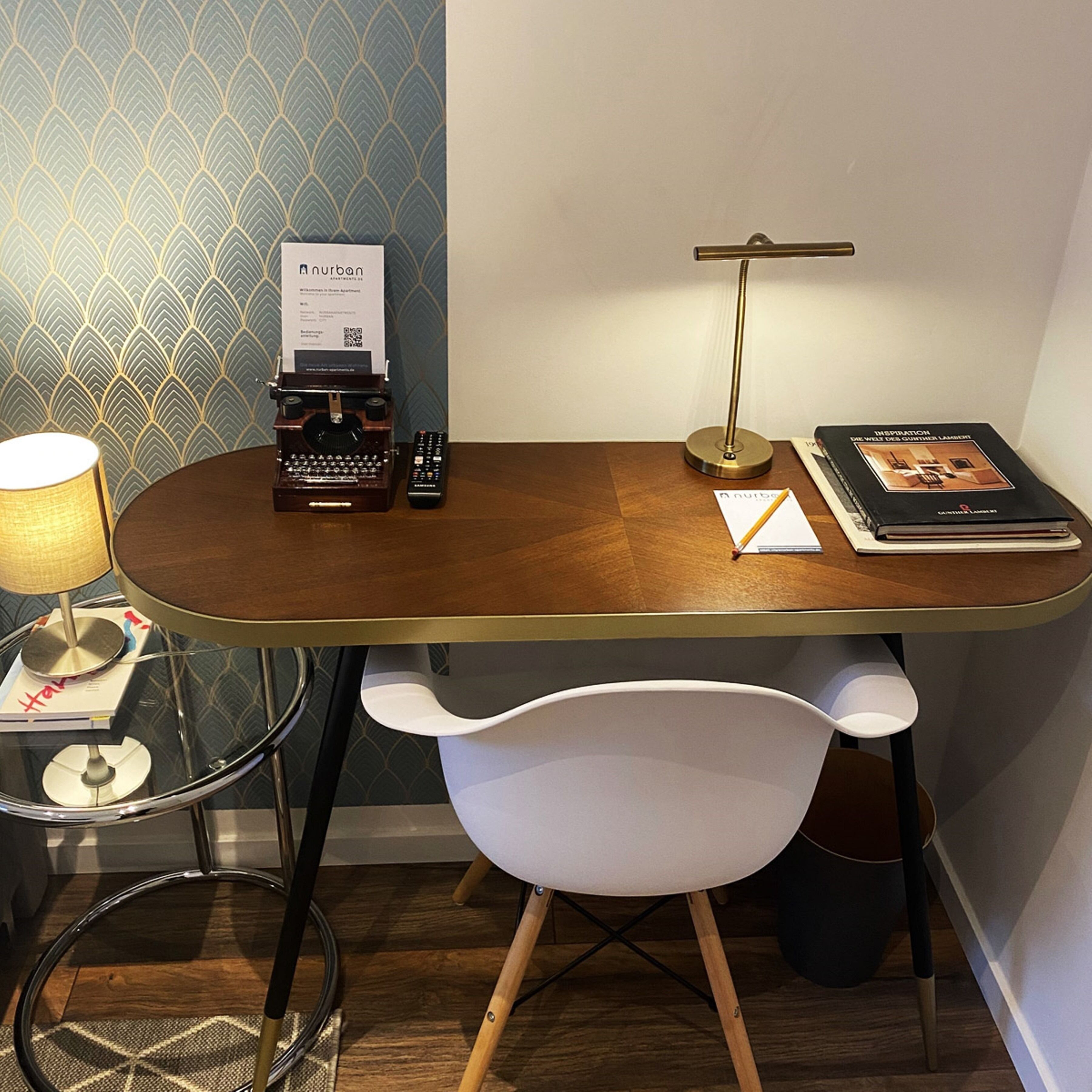 Un petit bureau moderne, avec un bureau en bois, une machine à écrire, une lampe, une télécommande et un livre.