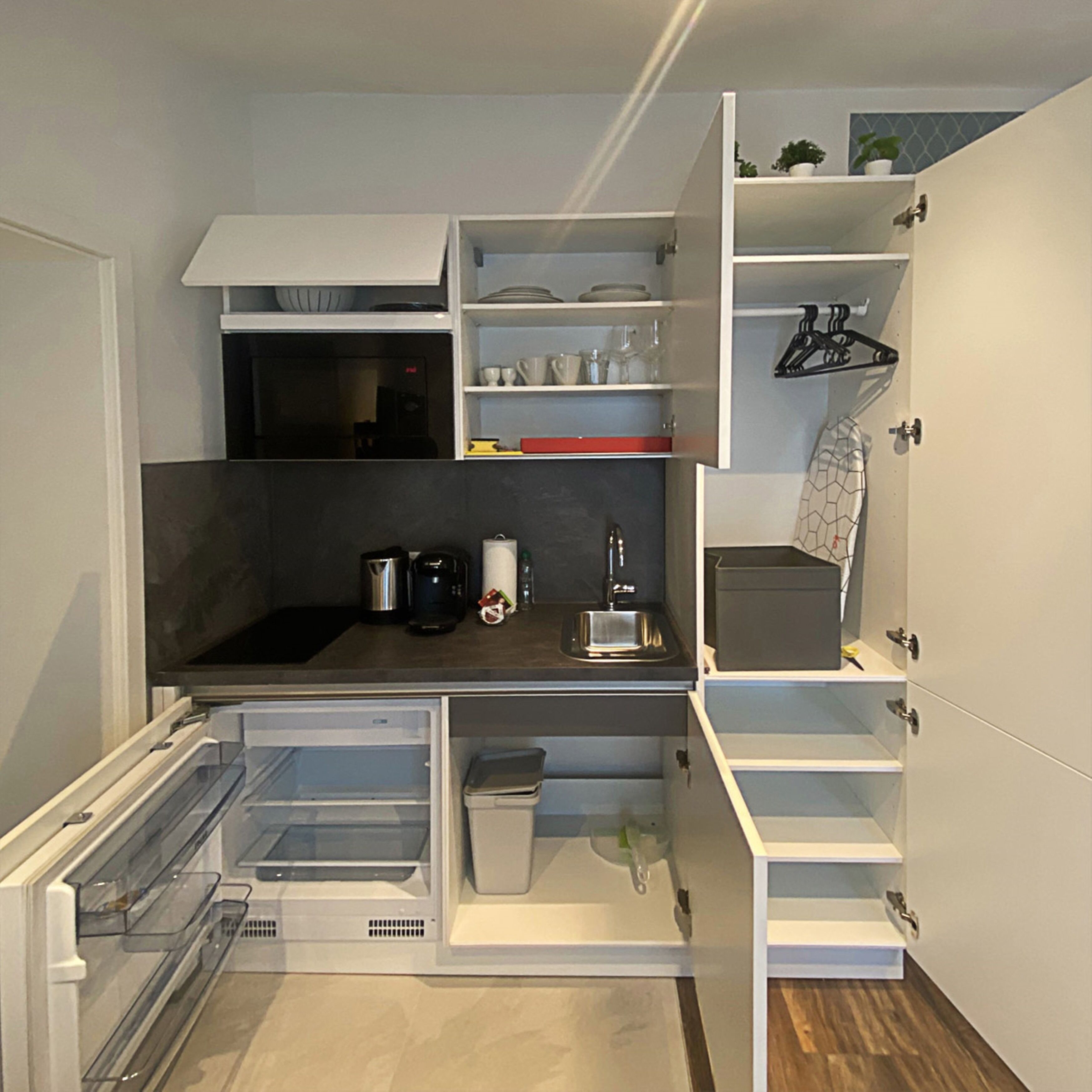 Una cocina compacta con electrodomésticos integrados, estanterías abiertas y una pequeña encimera.
