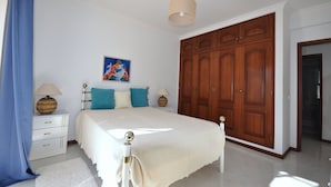 Une chambre à coucher avec une grande armoire en bois, un lit avec une literie blanche et deux tables de chevet avec des lampes.