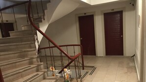 A staircase with a red handrail leading to a landing. There are two closed doors on the landing.