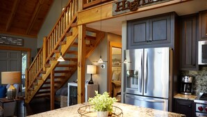 A kitchen with granite countertops, stainless steel appliances, and a wooden staircase. - Glen Falls Cottage: Hilltop Retreat w/ Deck, Covered Porch, Gas Fire Pit (Highlands)