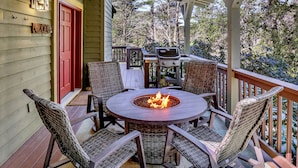 A covered outdoor patio with a round table and chairs, a fire pit, and a grill. - Glen Falls Cottage: Hilltop Retreat w/ Deck, Covered Porch, Gas Fire Pit (Highlands)