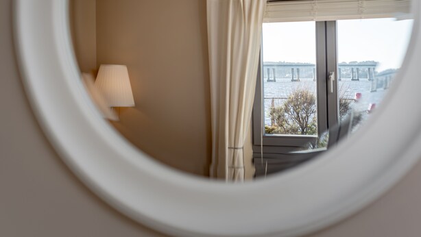 A room with a round window, a lamp, and a view of a bridge and trees outside.