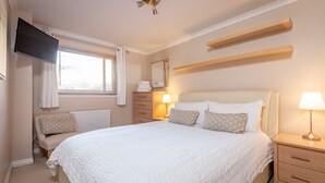 A bedroom with a large bed, bedside lamps, a TV mounted on the wall, and a window with curtains.