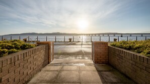 A concrete pathway leading to a waterfront with a metal railing and brick walls.