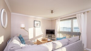 A living room with a grey sofa, a TV, and a window with blinds.