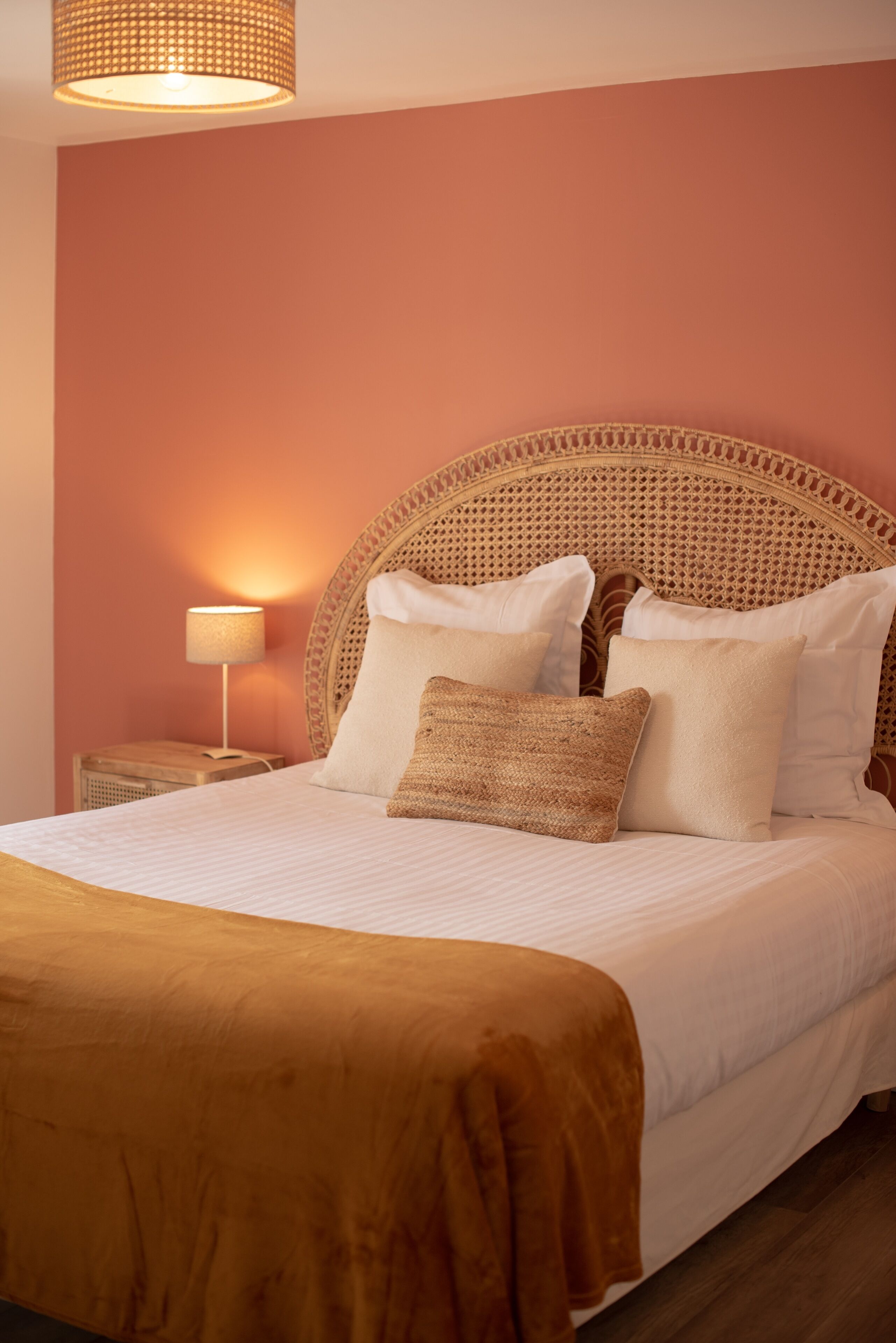 A neatly made bed with a woven headboard, a bedside lamp, and a brown throw blanket.