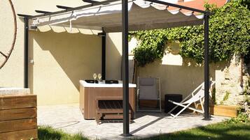 A covered outdoor seating area with a hot tub, wooden furniture, and a pergola.
