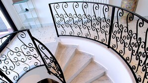 Un escalier en colimaçon avec des rampes en métal noir ouvragé et un mur blanc en arrière-plan.