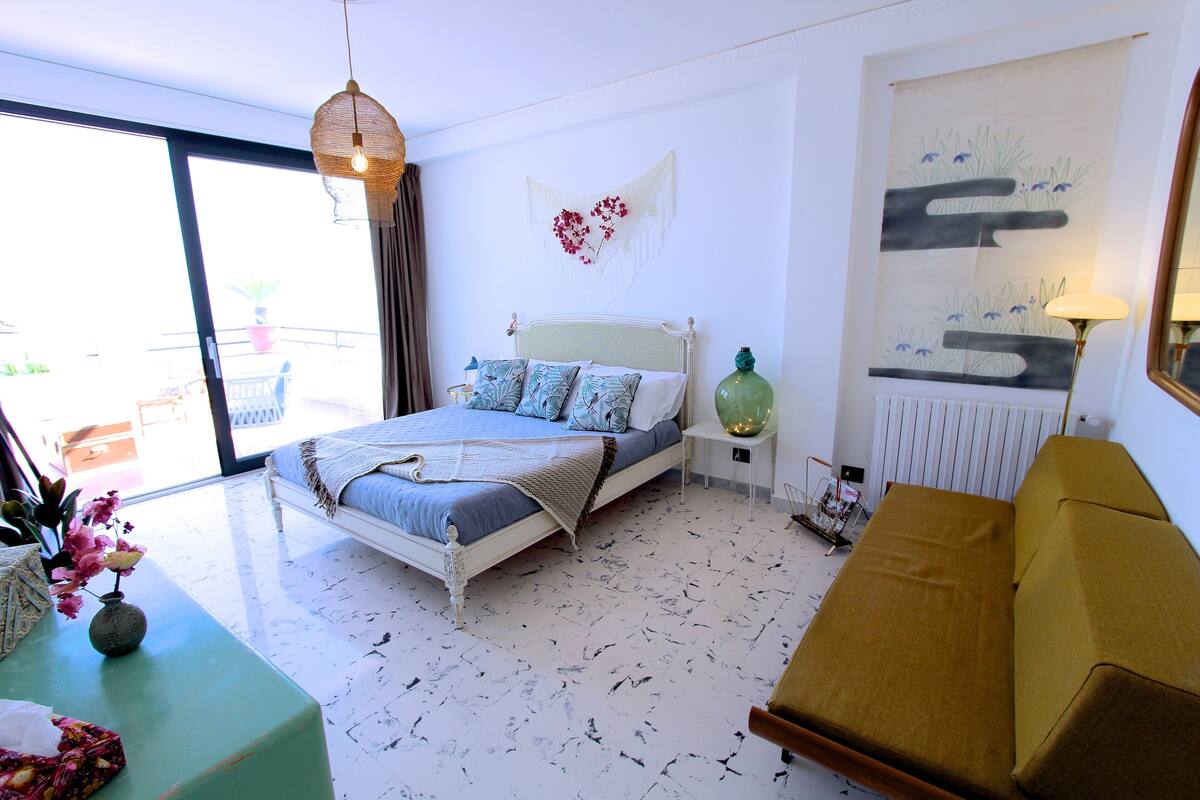 A bedroom with a bed, bedside table, and a view to the outside.