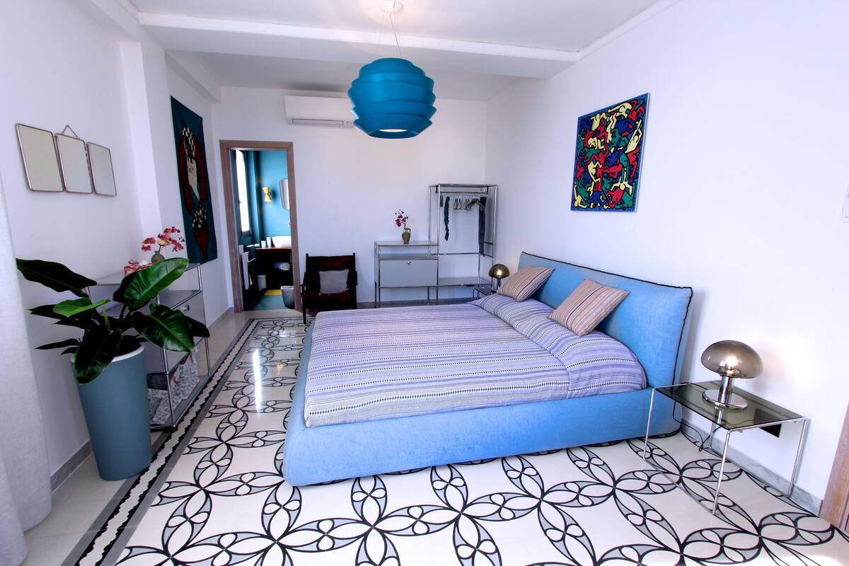 A modern bedroom with a large bed, a blue accent wall, and a decorative mirror.