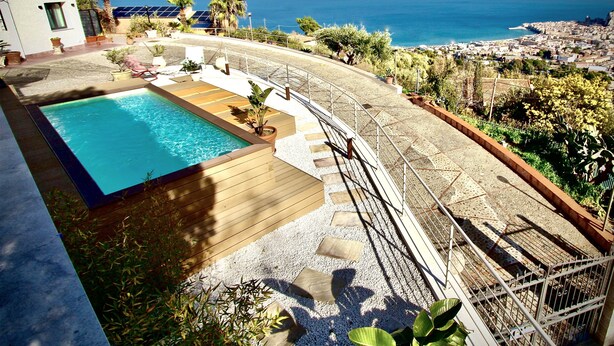 Un espace piscine avec vue sur l’océan, entouré de verdure et doté d’une terrasse dallée.