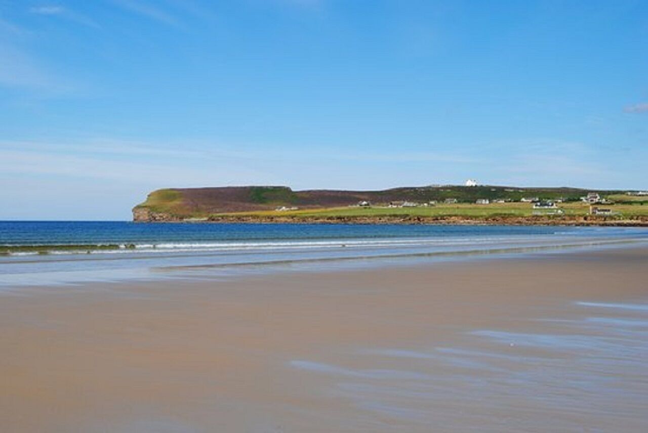 A beach with a cliff and houses in the background.