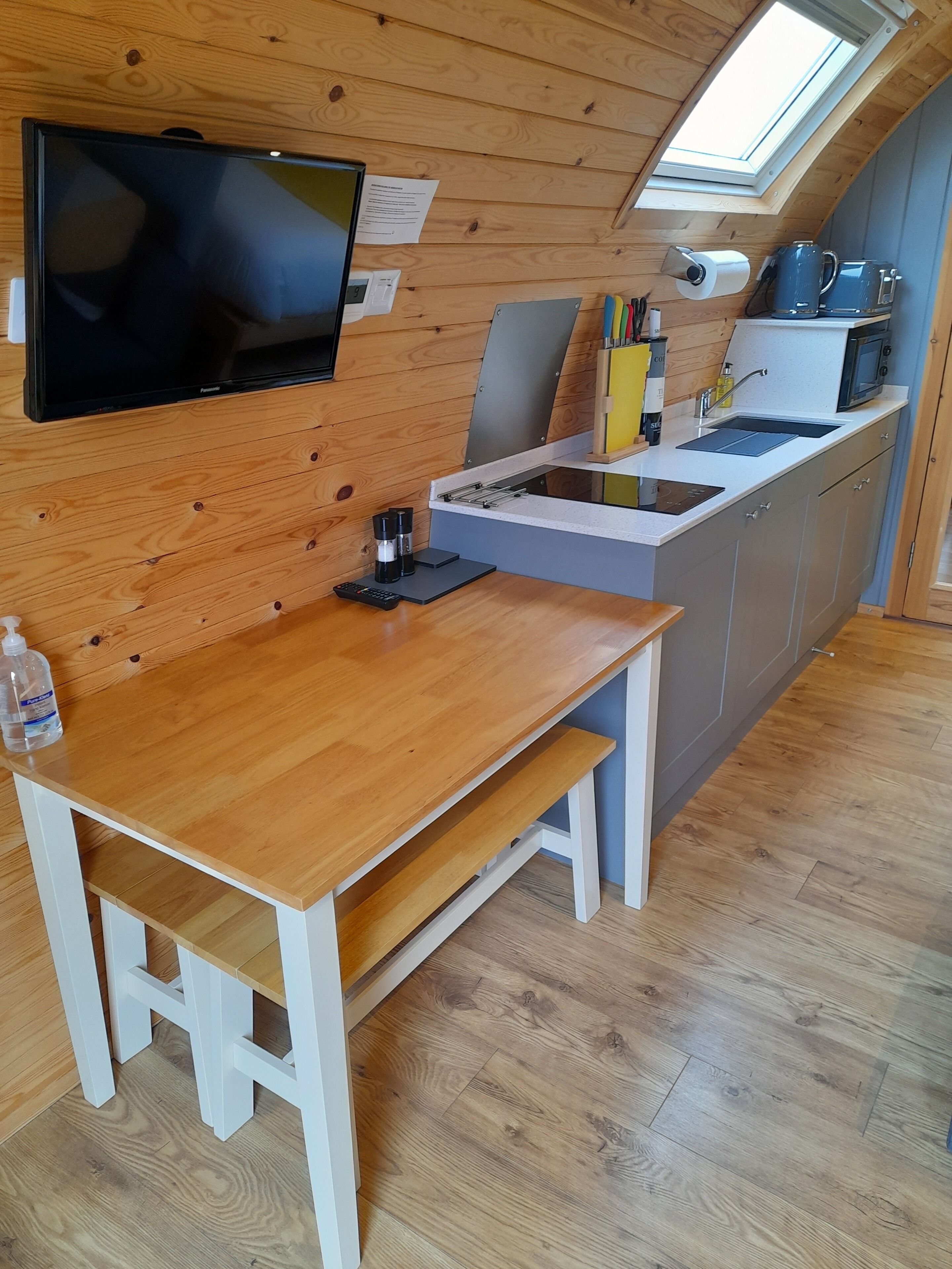 Cocina compacta con paredes de madera, televisor integrado, una pequeña mesa de comedor y un tragaluz.