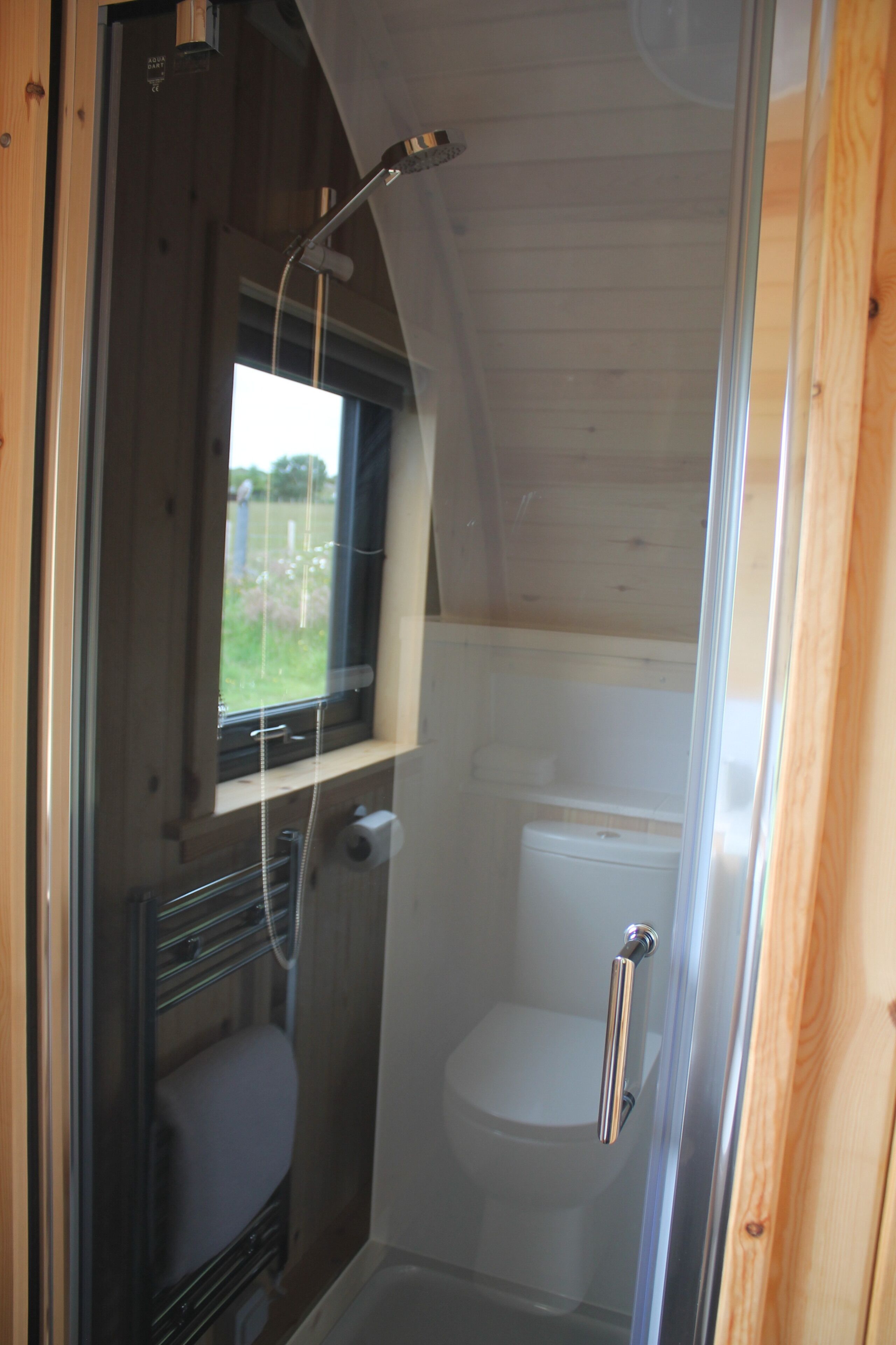 Une petite cabane compacte, composée d’une seule pièce, avec une douche, des toilettes et une petite fenêtre.