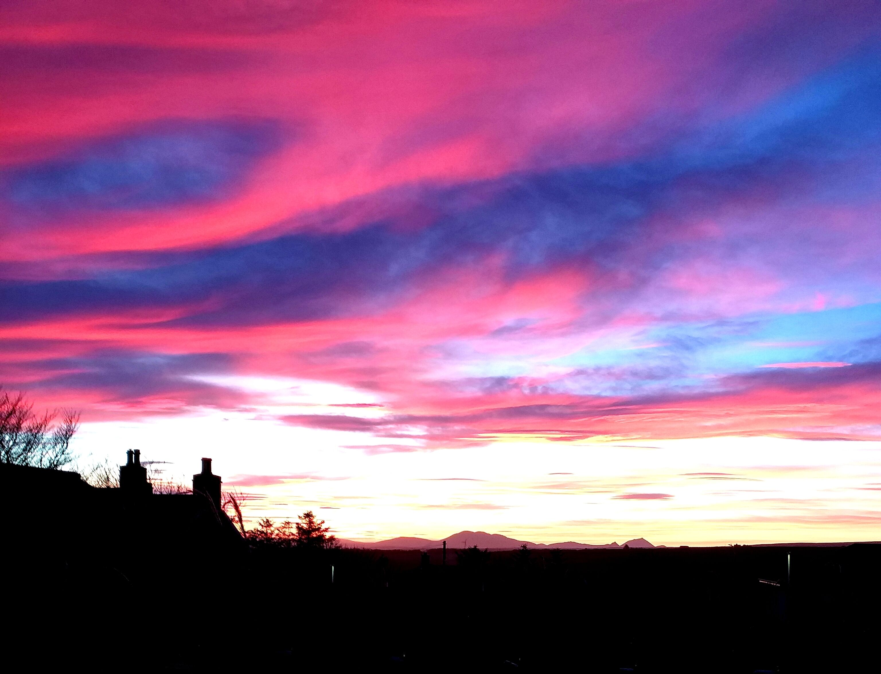 A sunset with vibrant pink and purple clouds over a silhouette of buildings and distant mountains.